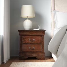 a nightstand with a lamp on top of it next to a bed in a bedroom