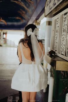 a woman in a white dress is standing near a wall and looking at the ceiling