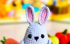 a small crocheted bunny sitting on top of a table next to carrots