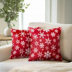 two red pillows sitting on top of a white couch next to a vase filled with flowers