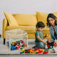 a woman and child playing with legos on the floor in front of a yellow couch