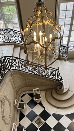 a chandelier hanging from the top of a stair case in a house with black and white checkered flooring