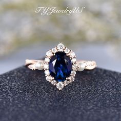 an oval shaped blue sapphire and pearl ring on top of a black surface with text overlay