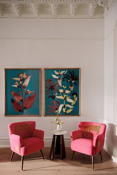 two red chairs sitting next to each other in front of paintings on the wall above them