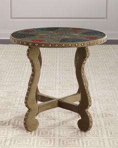 a small table with an ornate design on it's top and legs, sitting in front of a door