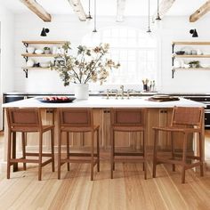 a kitchen with wooden floors and white walls, two stools at the center of the island