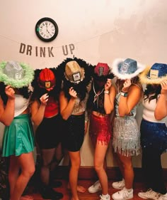 group of women in costumes standing next to wall with clock and drink up sign on it