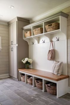 a white bench with baskets on it next to a wall mounted coat rack and cabinets