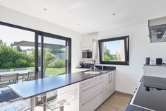 a kitchen with white cabinets and black counter tops next to a large window that looks out onto the backyard