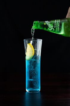 a person pouring water into a glass filled with blue liquid and lemon wedged in