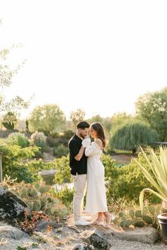 a man and woman standing next to each other in front of some cactus plants with their arms around each other