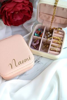 an open pink case with jewelry inside on a white sheet next to a red flower