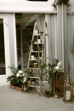 a wooden ladder with candles and flowers on the ground next to a glass door in front of a building