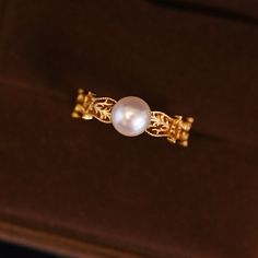 a pearl ring sitting on top of a velvet box with gold filigrees