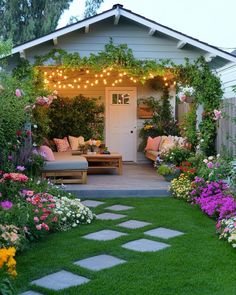 a garden with flowers and lights on the roof, in front of a white house