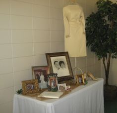 a table topped with pictures and framed photos next to a dress on a mannequin