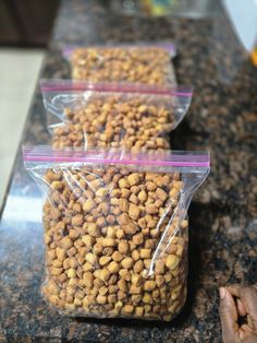 three bags of dog food sitting on top of a counter next to a person's hand