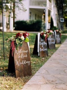 wooden signs that say welcome to our wedding are lined up on the grass in front of a house