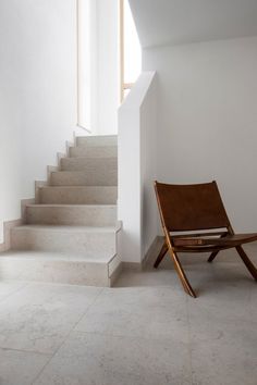 a wooden chair sitting in front of a set of stairs next to a white wall