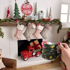 a person holding a coffee mug in front of a fireplace decorated with stockings and christmas trees