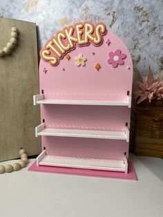 a pink shelf with stickers on it next to a wooden box and flower decoration