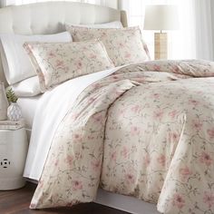 a bed with white sheets and pink flowers on the comforter is in front of a window