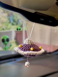 a small crocheted object hanging from the side of a car dashboard with an alien in the background