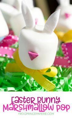 some bunny bunnies sitting on top of green shredded grass with pink and yellow bows