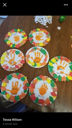 paper plates with handprints on them sitting on top of a wooden table next to leaves