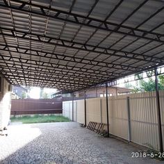 an empty parking lot next to a fence with benches under the pergolated roof