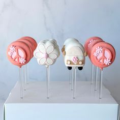 four cake pops with pink and white frosting on them, one decorated like a car