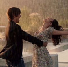 two people dancing in the rain with their arms around each other and one person holding an umbrella