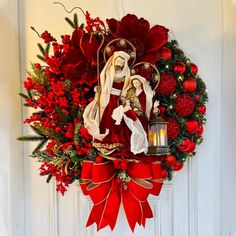 a wreath hanging on the front door decorated with red flowers and an image of virgin mary