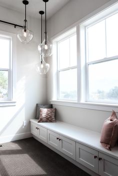 a room with some lights hanging from it's ceiling and two windows above the bench