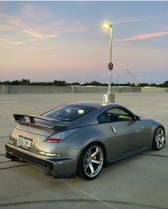 a silver sports car parked in an empty parking lot at dusk with the sun setting