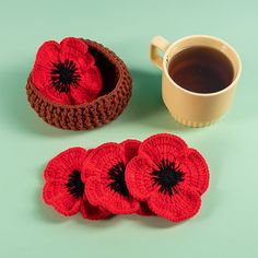 three crocheted red flowers sitting next to a cup of coffee on a green surface