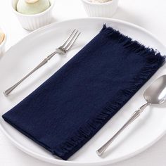 a white plate topped with a blue napkin and two silver spoons next to it