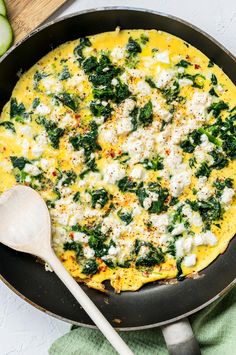 an omelet with spinach and cheese in a skillet next to sliced cucumbers