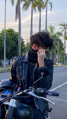 a man talking on his cell phone while riding a motorcycle down the street with palm trees in the background