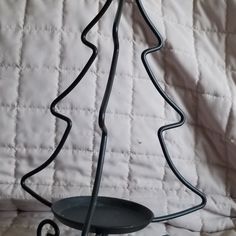 a small metal christmas tree sitting on top of a black plate next to a white quilt