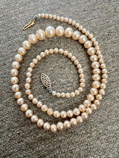 This gorgeous 17" strand of small to large to small faux pearls is perfect for special occasions or weddings. The pearls have a champagne color. The strand is secured by a decorative, vintage, hook and box fish hook clasp.  The necklace is in nice vintage condition. The pearls lack chippy or discoloration. Cream Single Strand Pearl Necklace, Formal Single Strand Cream Pearl Necklace, Formal Cream Single Strand Pearl Necklace, Elegant Single Strand Cream Pearl Necklace, Elegant Cream Single Strand Pearl Necklace, Classic Beige Jewelry For Formal Occasions, Beaded Pearl Necklace For Anniversary, Cream Pearl Necklace For Formal Occasions, Elegant Cream Beaded Necklaces For Formal Occasions