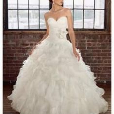 a woman in a white wedding dress standing next to a brick wall with windows behind her