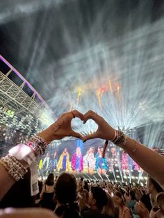 two hands making a heart shape with fireworks in the background at a music festival or concert