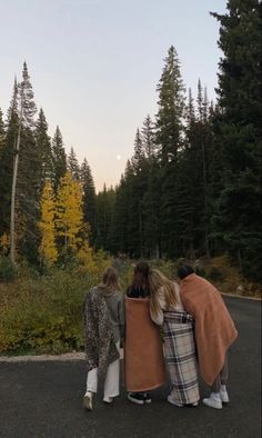 three people standing on the road with their backs to each other and looking at trees