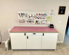 a white cabinet with pink counter top next to a wall hanging on it's side