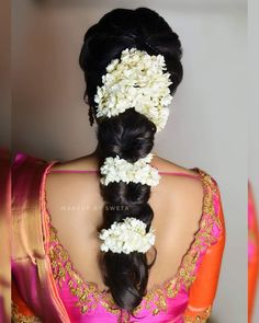 a woman with flowers in her hair wearing a pink and orange saree, looking back