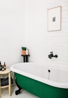 a white brick wall in a bathroom with green bathtub and small table next to it