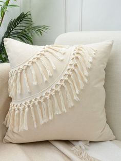 a white pillow with tassels on it sitting on a couch next to a potted plant