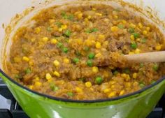 a green pot filled with food on top of a stove next to a wooden spoon