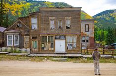 a man standing in front of an old wooden house on the side of a road